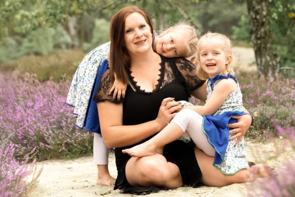 Mama und ihre Kinder Lächelnde Mutter sitzt mit ihren beiden kleinen Kindern im Freien und hält sie liebevoll im Arm.