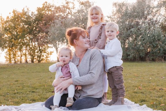 Liebevolle Familienmomente Mutter sitzt mit drei kleinen Kindern eng zusammen auf einer Wiese im warmen Sonnenlicht.