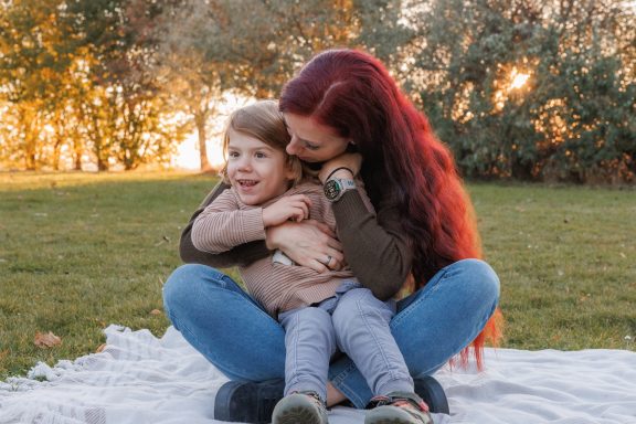 Innige Momente zwischen Mutter und Kind Mutter mit roten Haaren sitzt auf einer Wiese und umarmt ihr Kind liebevoll.
