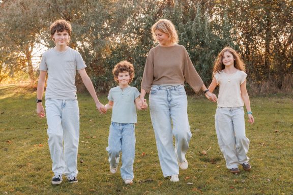 Gemeinsam durch die Natur Mutter geht mit ihren drei Kindern Hand in Hand über eine grüne Wiese.