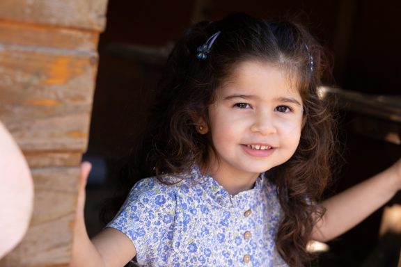 Mädchen mit dunklen Locken lächelt bei einem natürlichen Kinderporträt