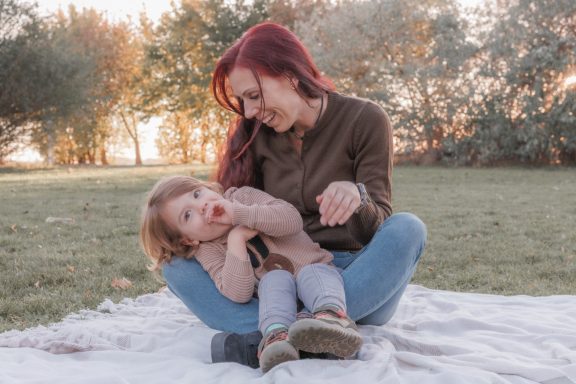 Kuschelmomente beim Familienshooting Mutter sitzt auf einer Decke im Grünen und schaut liebevoll zu ihrem Kind, das sich an sie kuschelt.