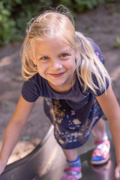 Blondes Mädchen lächelt bei einem natürlichen Outdoor-Kinderporträt